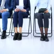Groupe de professionnels assis dans un bureau, attendant un entretien d'embauche tout en utilisant des appareils électroniques.