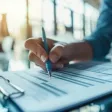 Employée concentrée, rédigeant son auto-évaluation professionnelle sur son ordinateur portable, entourée de documents et graphiques colorés.