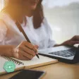 Une femme devant son ordinateur qui prend des notes sur un cahier