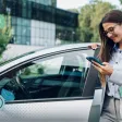 Une femme sort de son véhicule professionnel et regarde son téléphone en souriant