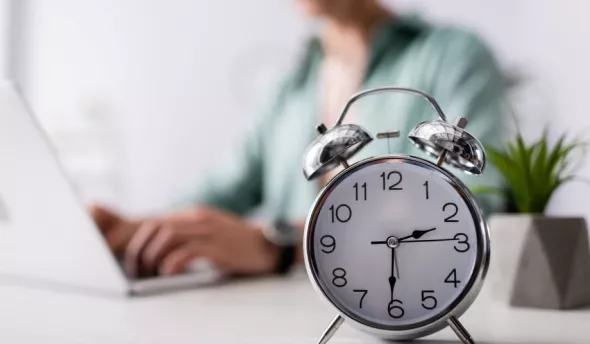 Une femme sur son ordinateur en arrière plan et un réveil en premier plan