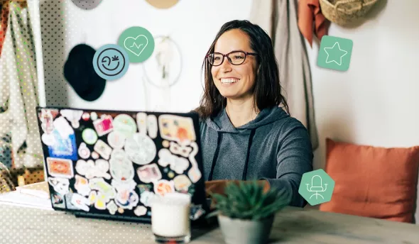 Jeune femme souriante tapant sur un ordinateur portable décoré de stickers, dans un coin de travail chaleureux.