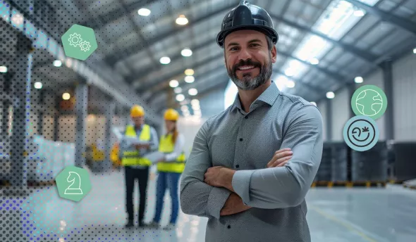 Souriant chef d’entreprise au casque et bras croisés dans un atelier moderne, équipe floue en arrière-plan
