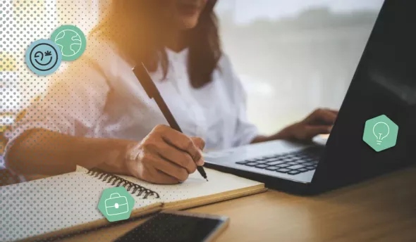Une femme devant son ordinateur qui prend des notes sur un cahier