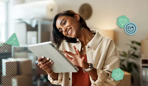 Jeune femme souriante discute au téléphone tout en consultant sa tablette dans son atelier