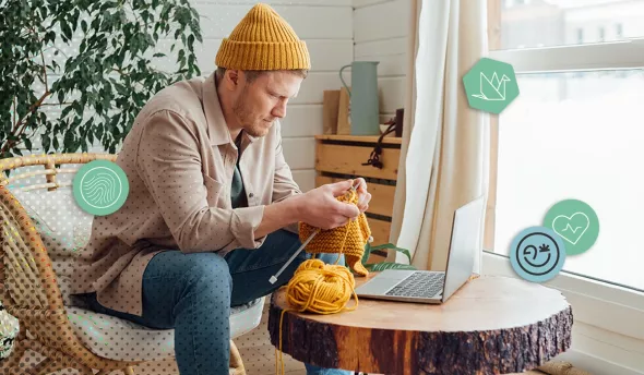 Homme tricotant un pull jaune devant son ordinateur portable dans un espace cosy
