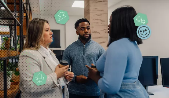 Trois collègues discutent calmement dans un open space moderne, chacun tenant un café