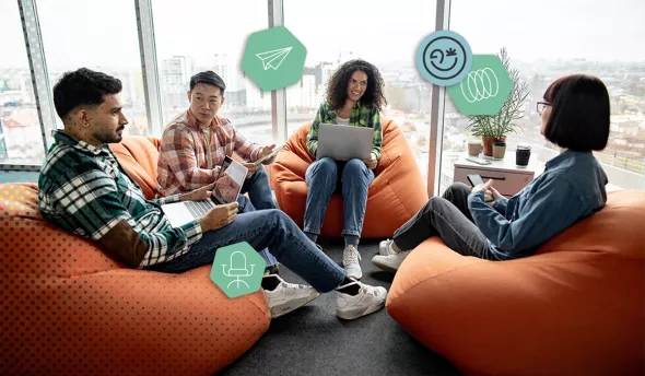 Réunion informelle entre jeunes collègues sur des poufs, avec ordinateurs et smartphones.