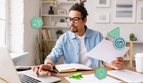 Homme concentré travaillant sur ordinateur avec des papiers à son bureau avec une grenouille verte en origami et une tasse à café
