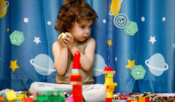Enfant assis jouant avec des jouets colorés devant un rideau décoré d'étoiles et planètes
