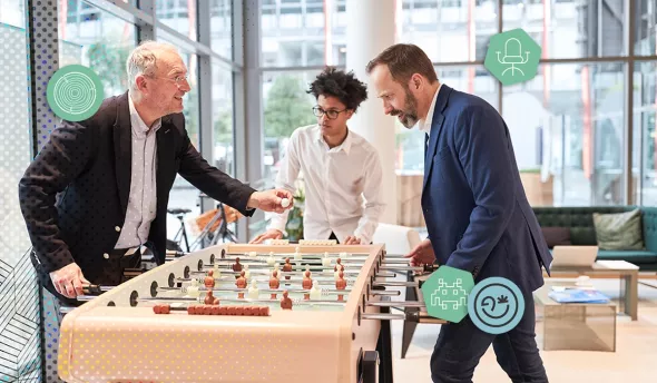 Collègues de différentes générations jouant au babyfoot dans l’espace détente de l’entreprise