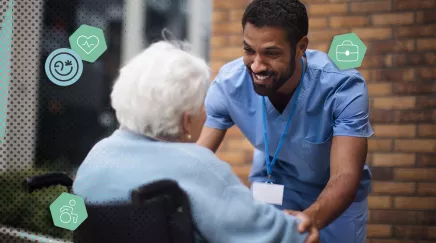 Aidant souriant échange avec une personne âgée en fauteuil roulant devant un bâtiment.