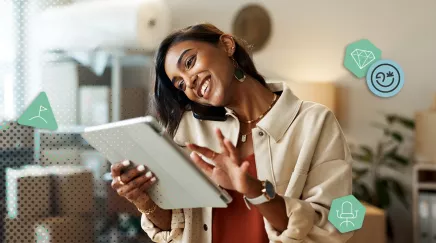 Jeune femme souriante discute au téléphone tout en consultant sa tablette dans son atelier