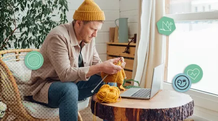 Homme tricotant un pull jaune devant son ordinateur portable dans un espace cosy