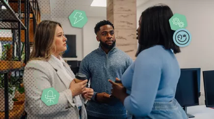 Trois collègues discutent calmement dans un open space moderne, chacun tenant un café