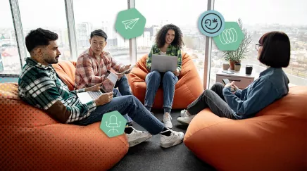 Réunion informelle entre jeunes collègues sur des poufs, avec ordinateurs et smartphones.