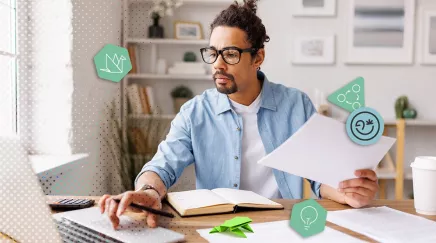 Homme concentré travaillant sur ordinateur avec des papiers à son bureau avec une grenouille verte en origami et une tasse à café