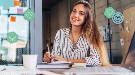 Femme souriante rédigeant des notes sur un carnet, ordinateur et tasse de café à portée de main.