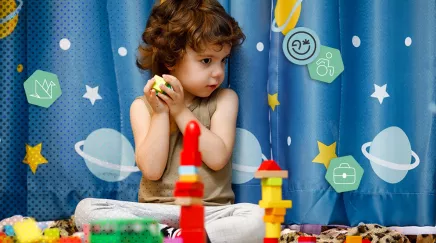Enfant assis jouant avec des jouets colorés devant un rideau décoré d'étoiles et planètes