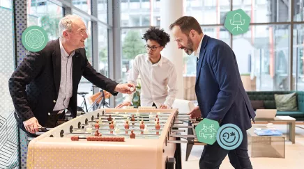 Collègues de différentes générations jouant au babyfoot dans l’espace détente de l’entreprise